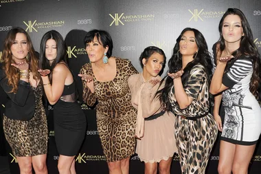 Women posing and blowing kisses at Kardashian Kollection launch event backdrop.