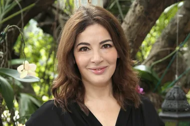 A woman with shoulder-length brown hair smiling outdoors with greenery in the background.