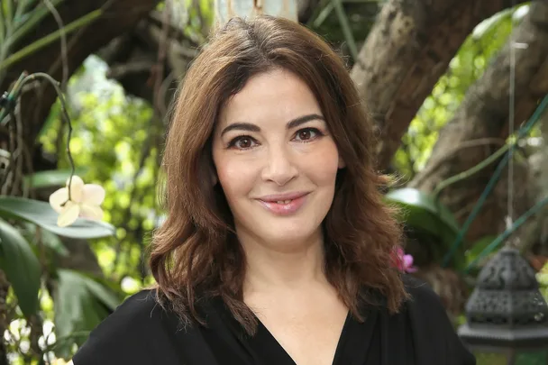 A woman with shoulder-length brown hair smiling outdoors with greenery in the background.