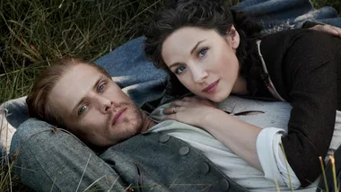 Couple lying in grass, gazing upward; woman rests her arm on man's chest.