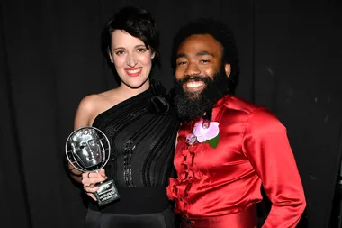 Two people smiling, one holding a BAFTA award, against a black background.