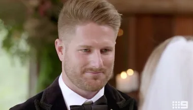Man in formal attire with a bow tie smiling at someone in a veil during a wedding ceremony, indoors.