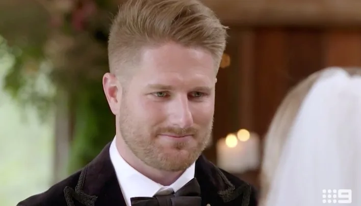 Man in formal attire with a bow tie smiling at someone in a veil during a wedding ceremony, indoors.