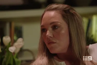 A woman with long hair looks to the side in a dimly lit room with flowers in the background; Nine Network logo visible.