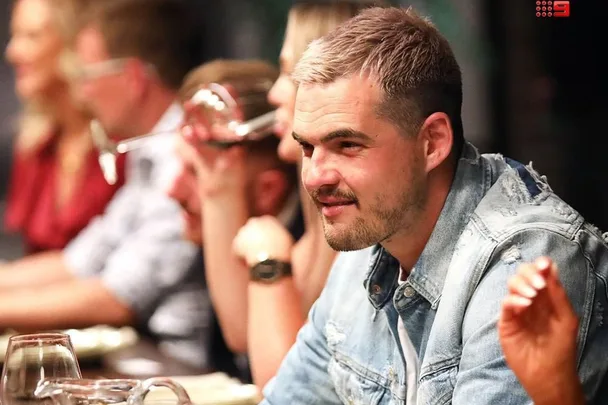 A group of people seated at a table, one man in focus wearing a denim jacket.