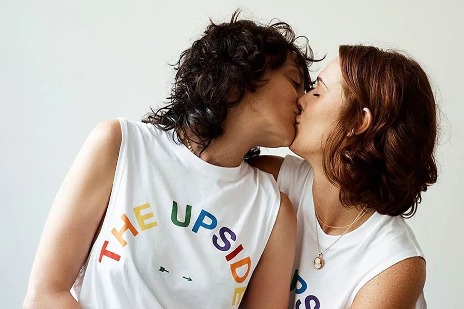 Two people kissing, wearing matching white shirts with the rainbow text "THE UPSIDE".