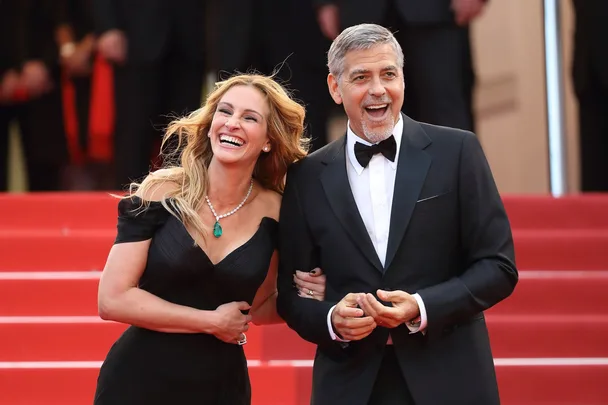 Two people smiling and posing on a red carpet, dressed in elegant formal attire.