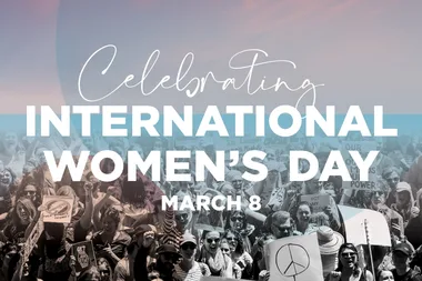 Celebrating International Women's Day on March 8 with a crowd holding signs in the background.