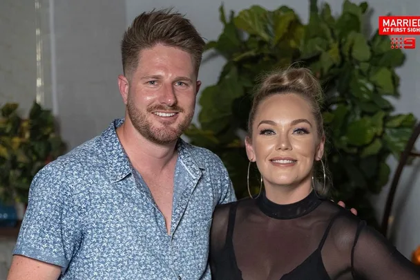 Man in blue floral shirt and woman with updo smile at camera, "Married at First Sight" logo in corner.