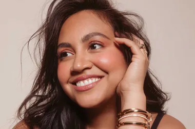 Smiling person with long dark hair and gold bracelets, gazing upwards.