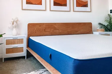 Modern bedroom with a wooden bed frame, a blue mattress, white side tables, and artwork on the wall.