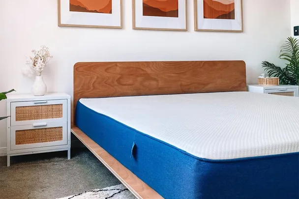 Modern bedroom with a wooden bed frame, a blue mattress, white side tables, and artwork on the wall.