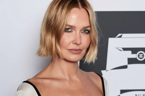 A person with short blonde hair poses in front of a black and white background.