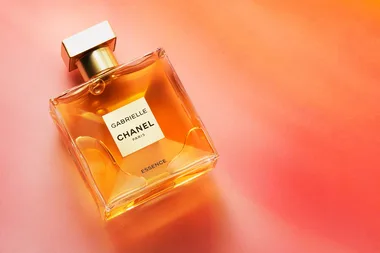 Gabrielle Chanel Essence perfume bottle on a gradient orange background.