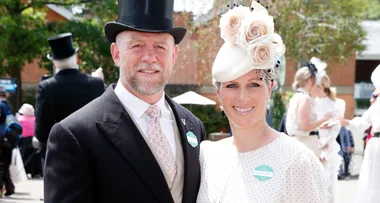A couple dressed in formal attire and hats at an outdoor event, smiling at the camera.