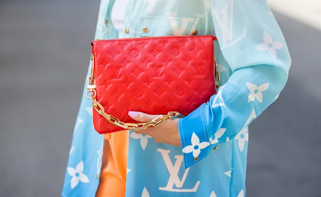 Person holding a red Louis Vuitton clutch with gold chain, wearing a blue patterned shirt.
