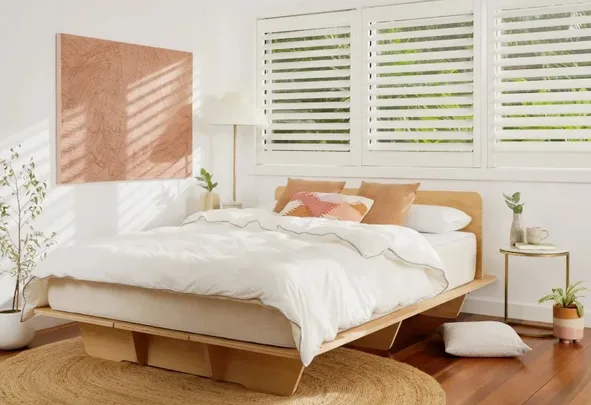 Modern bedroom with a wooden platform bed, white bedding, pillows, artwork, and large windows with shutters.