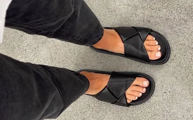 Person wearing black crisscross sandals and black pants on gray concrete floor.