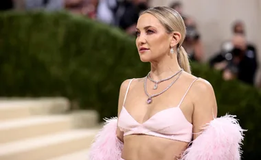 ```html
<img src="image-url" alt="Person in pink outfit with feathered shawl and layered necklaces at a formal event." />
```