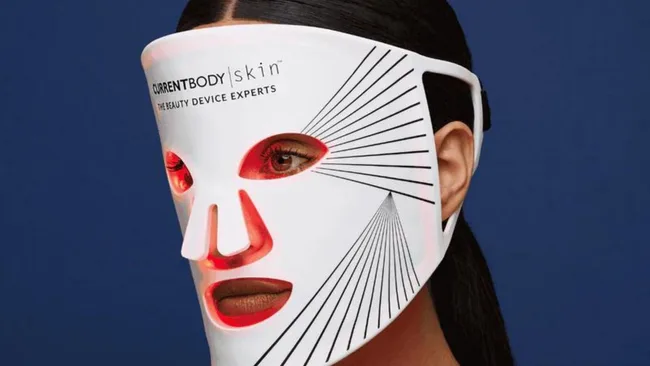 Person wearing a CurrentBody Skin LED mask with red lights, against a blue background.