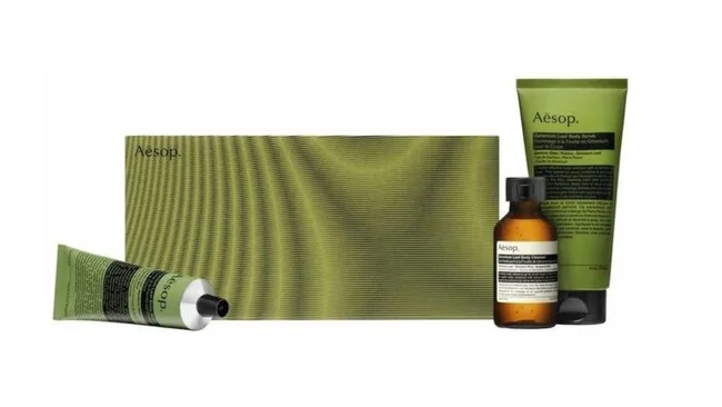 Aesop skincare set with a green tube, small amber bottle, and rectangular box.