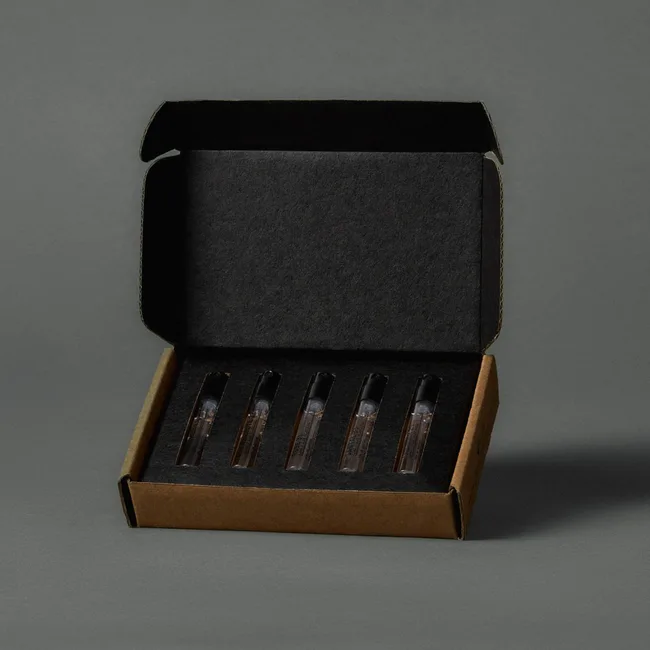 Box containing five small transparent vials with black caps, placed in individual slots on a dark cushion.