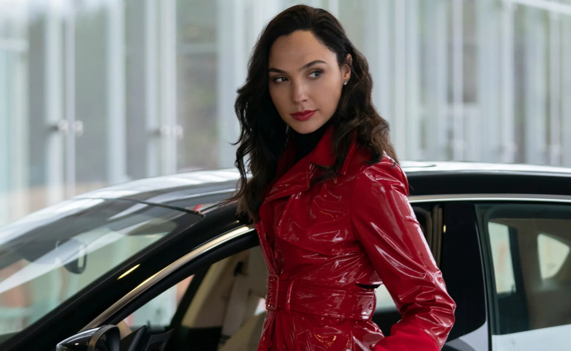 A woman in a red coat standing beside a car, looking to the side with a confident expression.