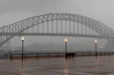 Sydney Harbour Bridge on a rainy day with streetlights and wet pavement in the foreground.