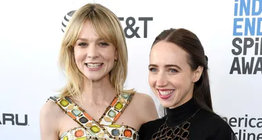 Two women smiling at an event, one wearing a colorful dress, the other in a black top, with logos in the background.