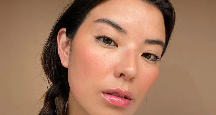 Young woman with braided hair and natural makeup against a plain background, close-up portrait.