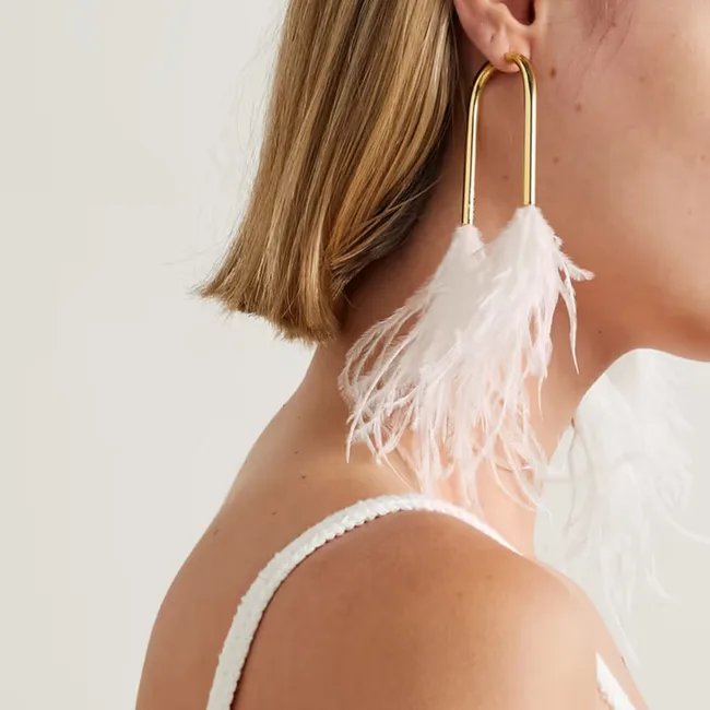 Woman with short hair wearing a large gold hoop earring adorned with white feathers.