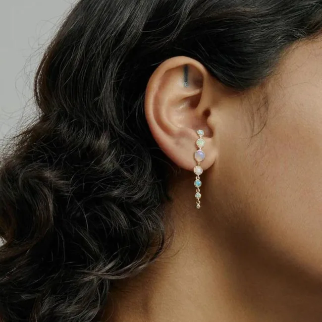 A woman's ear wearing a gold earring with multiple round, pastel-colored gemstones against a neutral background.