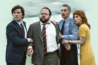 Four people in office attire stand closely, looking in the same direction with concerned expressions.