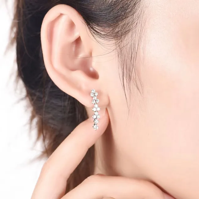 Woman wearing a sparkling diamond drop earring, touching it gently with her finger.