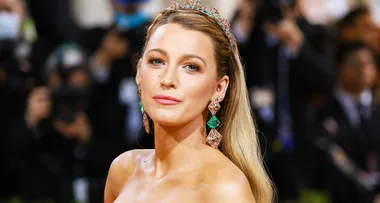 Woman in a strapless gown with long earrings and hairpiece, posing on a formal event red carpet with photographers.