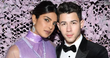 Two people pose in formal attire against a backdrop of purple leaves.