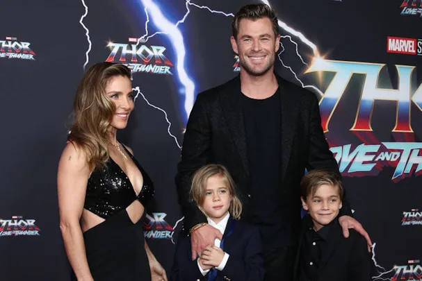 Family poses at the "Thor: Love and Thunder" premiere, with movie title and electric graphics in the background.