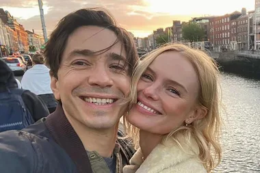 A man and woman smiling together outdoors near a river at sunset.