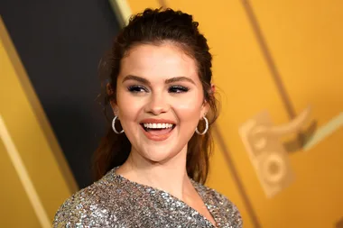 A woman in a sparkly silver outfit smiling at an event with a golden background.