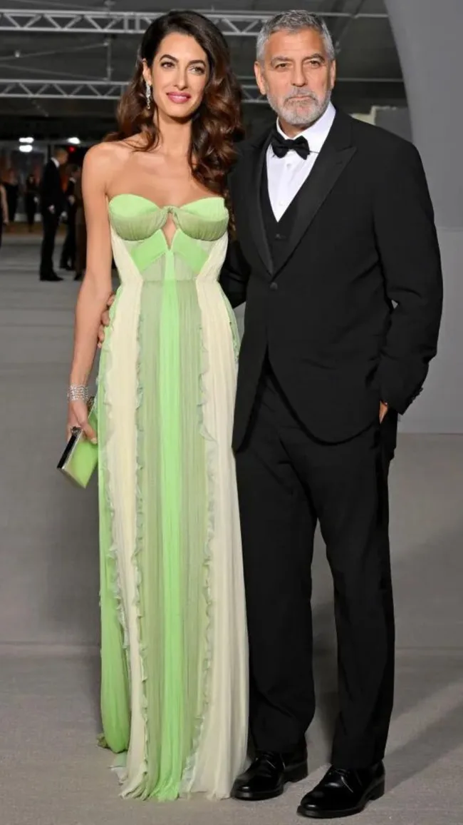 Elegant couple in formal attire; woman in a green gown, man in a black tuxedo, posing at an event.