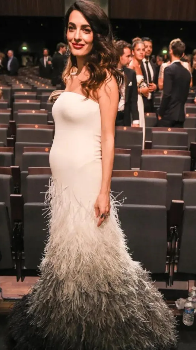 Elegant woman in a strapless white gown with feathered skirt standing in an auditorium.