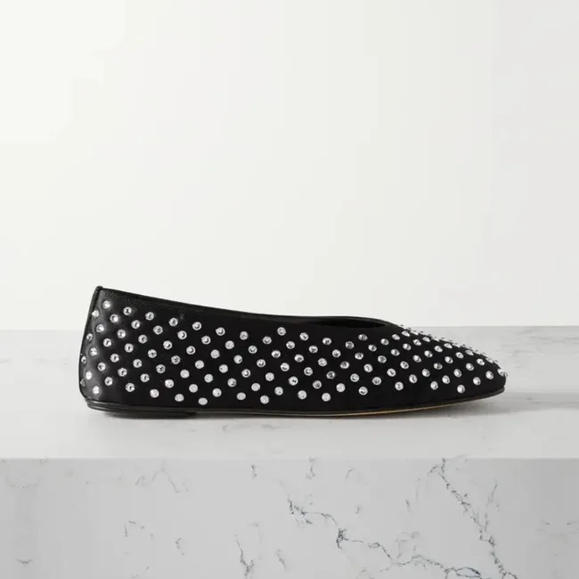 Black flat shoe with silver studs on a marble surface.