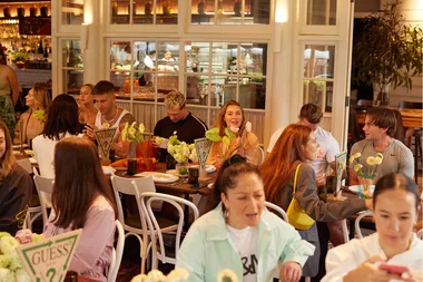 A group of people seated around tables in a cozy restaurant setting decorated with flowers.