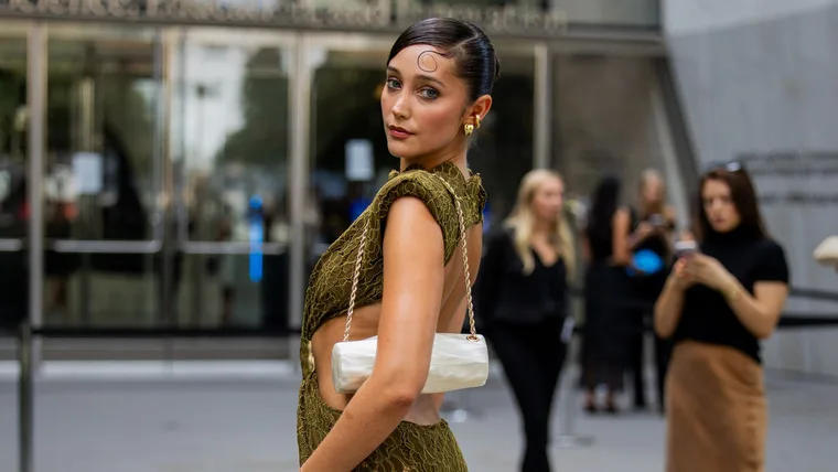 Wedding guest carries mother of pearl shoulder bag with gold strap and wears green backless dress
