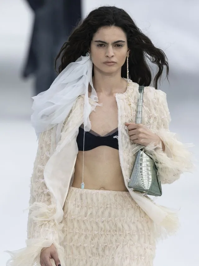 Model at Dior SS27 runway wears black bralette beneath cream jacket