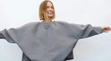 Woman in oversized gray outfit smiling with arms outstretched against a plain white background.