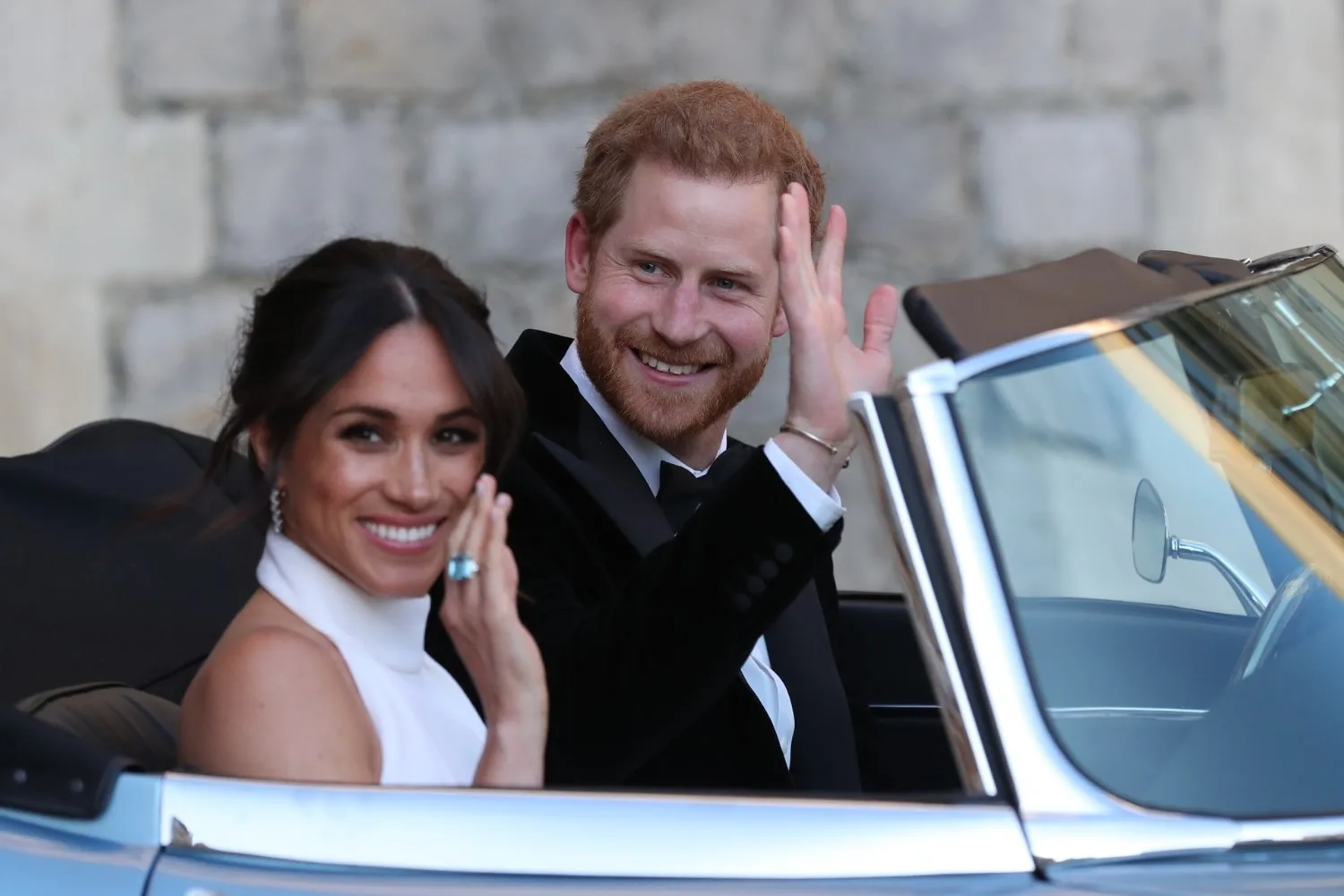 Couple smiling and waving from a convertible car.