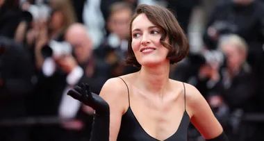 A woman in a black dress posing on a red carpet with photographers in the background.