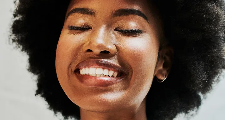 Smiling person with closed eyes and natural afro hairstyle.