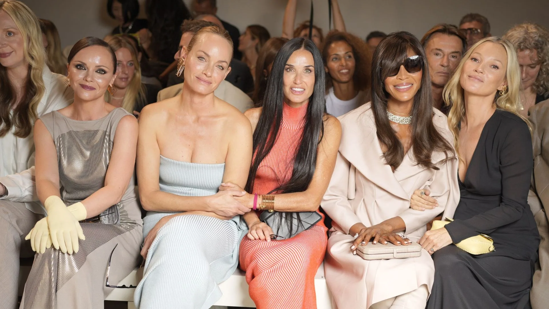 Group of women sitting at a fashion event, smiling. Some wearing elegant dresses and accessories.